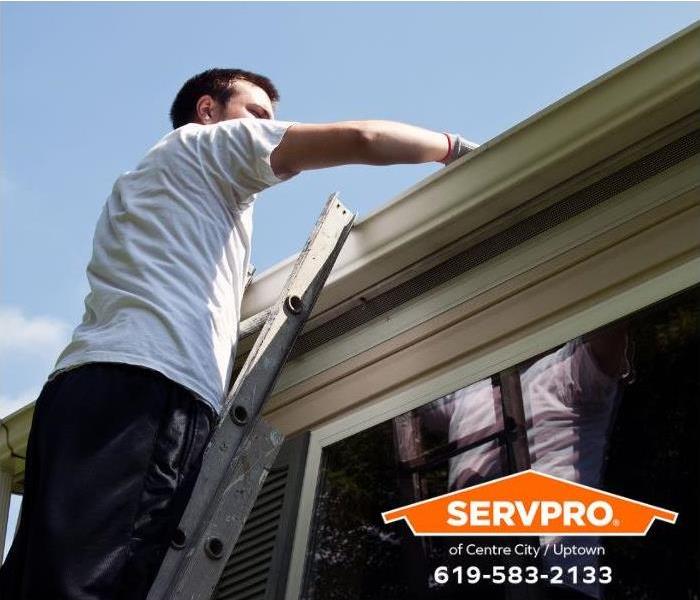 A person is cleaning leaves from a roof gutter.