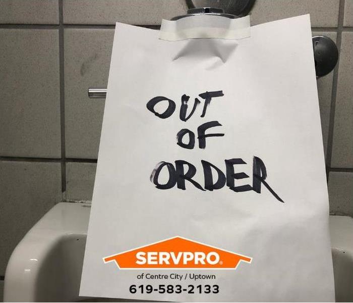 A hand-written “out of order sign” is taped to a toilet in a public restroom. 