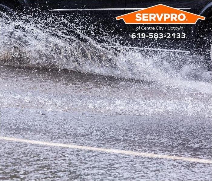 A car splashes through a large puddle on a wet road.